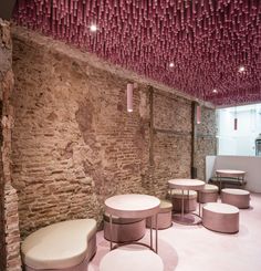 a room with several tables and stools in front of a brick wall that has pink ribbons hanging from the ceiling