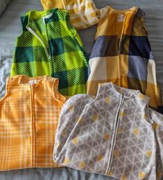 five baby clothes laid out on top of a bed next to each other, all in different colors