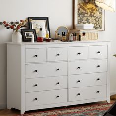 a white dresser with lots of drawers and pictures on it's top shelf in a living room