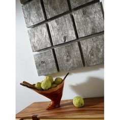 a wooden bowl filled with green fruit sitting on top of a table next to a piece of wood