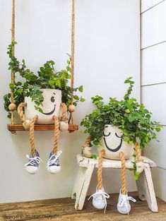 two potted plants with faces drawn on them are hanging from wooden ladders in front of a white wall