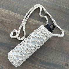 a white crocheted water bottle on a wooden floor with a black plastic cap