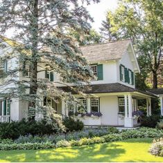 a white house with green shutters on the front and side windows, surrounded by trees