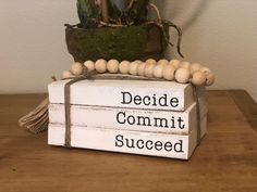 a wooden sign that says decide commit succed and sits on a table next to a potted plant