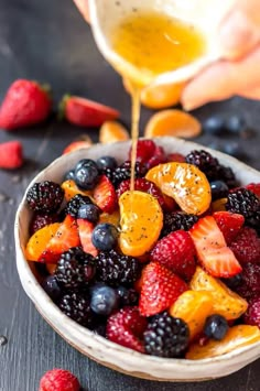 someone pouring orange juice into a bowl of mixed berries and raspberries for a fruit salad