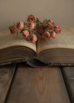 an open book sitting on top of a wooden table filled with pink flowers and leaves