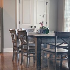 a dining room table with four chairs and a vase on top of it in front of a door