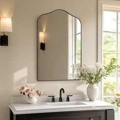 a bathroom sink with a mirror above it and flowers in vases on the counter