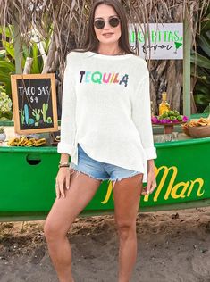 Tequila is always the life of the party! Soft, lightweight and breathable cotton blend top featuring the word "Tequila" knit directly into the center front. A different festive color yarn is used for each letter. The boxy body is knit in a flattering, slouchy shape. Composition: 60% cotton, 40% acrylic Fun Long Sleeve Tops For Vacation, White Stretch Sweater For Vacation, White Crew Neck Sweater For Beach, White Crew Neck Sweater For Summer, White Crew Neck Top For Brunch, Trendy White Summer Sweater, Casual White Sweater For Brunch, White Graphic Print Tops For Cinco De Mayo, White Letter Print Tops For Cinco De Mayo