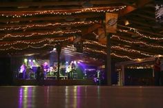 a band playing on stage in a large room with lights strung across the ceiling and wooden beams