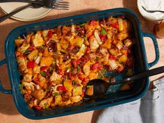 a blue casserole dish filled with chicken and vegetables next to utensils