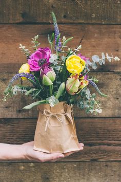 a person holding a paper bag with flowers in it on top of a wooden table