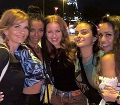 four girls are posing for the camera in front of a city street at night with their arms around each other