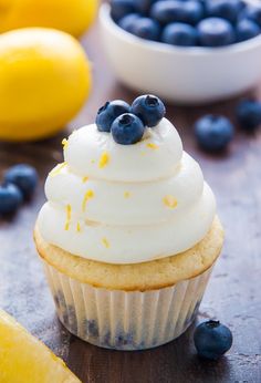 a cupcake with white frosting and blueberries on top next to lemons