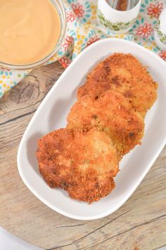 two pieces of fried food in a white dish on a wooden table with dipping sauce