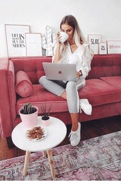 a woman sitting on a couch drinking coffee and using a laptop computer while holding a cup