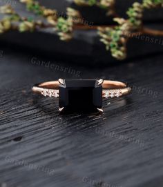 an engagement ring with a black stone surrounded by white diamonds on a wooden table next to plants