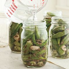 three mason jars filled with green beans and other things to eat on the table in front of them