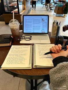 a person sitting at a table with a notebook and pen in front of a laptop