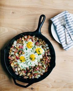 an iron skillet with eggs and potatoes in it next to a plate of silverware