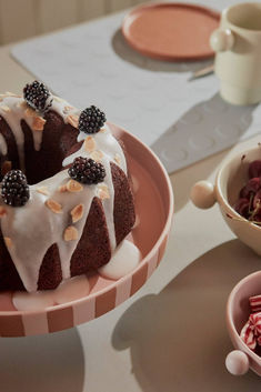 a bundt cake with white icing and blackberries on top sits in a pink plate