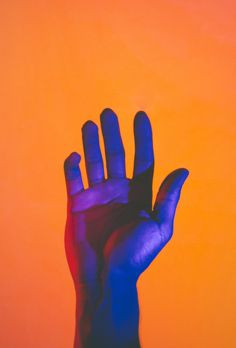 a person's hand with their fingers up against an orange and blue background stock photo