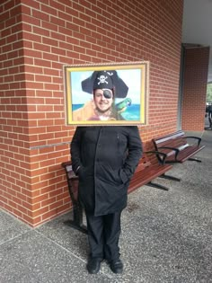 a man standing in front of a brick wall holding up a painting with a pirate on it