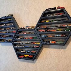 three black hexagonal shelves filled with toy cars on top of a floor next to a wall