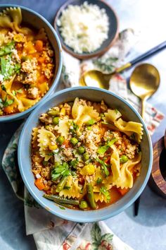 two bowls filled with pasta and vegetables next to spoons