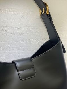 a black leather bag hanging on a wall with a gold buckle and strap around it