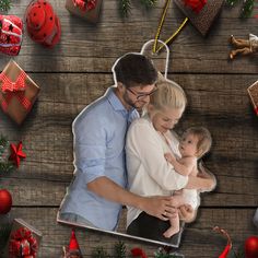 a man and woman are holding a baby in front of christmas decorations on a wooden table