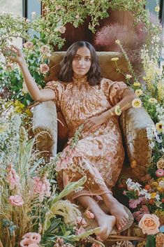 a woman is sitting in a chair surrounded by flowers and greenery with her arms outstretched