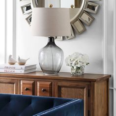 a table with a lamp, mirror and vase on it next to a blue couch