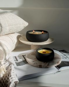 two black bowls with candles in them sitting on a table next to a white towel