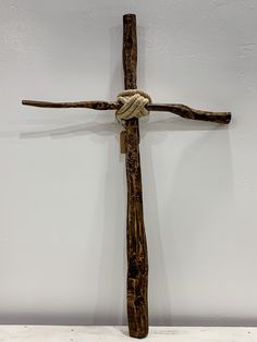 a wooden cross with rope hanging from it's sides on a white wall in a room