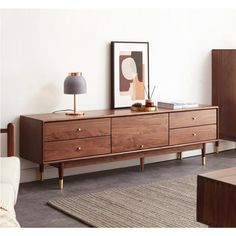 a wooden dresser with two lamps on top of it next to a couch and table