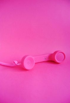 a pink telephone on a pink background with the phone cord up to it's ear