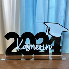 a clear acrylic sign with the words karmenn and a graduation cap on it