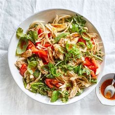 a white bowl filled with pasta and vegetables next to a small container of dressing sauce