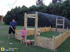 a man and two children standing in front of a wooden garden bed with netting over it