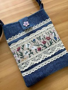 a purse made out of old jeans with lace and flowers on the side, sitting on a wooden table