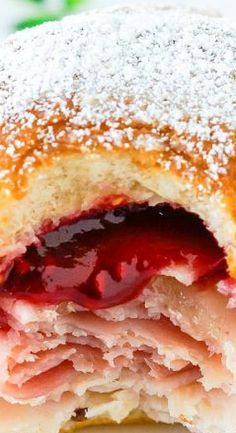 a strawberry filled pastry with powdered sugar and jelly on the inside, cut in half