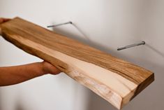 a person holding a piece of wood with nails on the wall in front of them