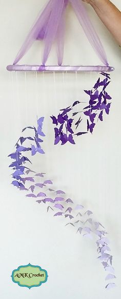 a person is holding a purple and white paper mobile with flowers on it, in front of a white wall