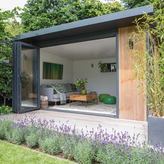 an outdoor living area with furniture and flowers in the foreground, surrounded by greenery