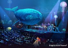 a large blue whale is in the middle of an auditorium full of people and jelly fish