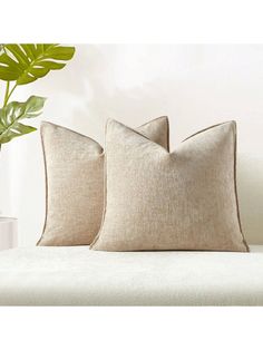 two pillows sitting on top of a white couch next to a potted green plant