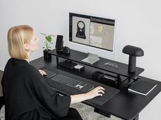 a woman sitting at a desk with a computer monitor and keyboard in front of her