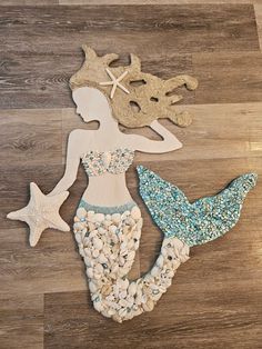 three wooden cutouts of mermaid, starfish and shell shapes on a wood floor