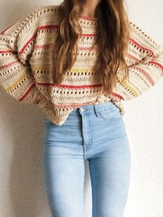 a woman wearing jeans and a sweater standing next to a wall with her hands on her hips